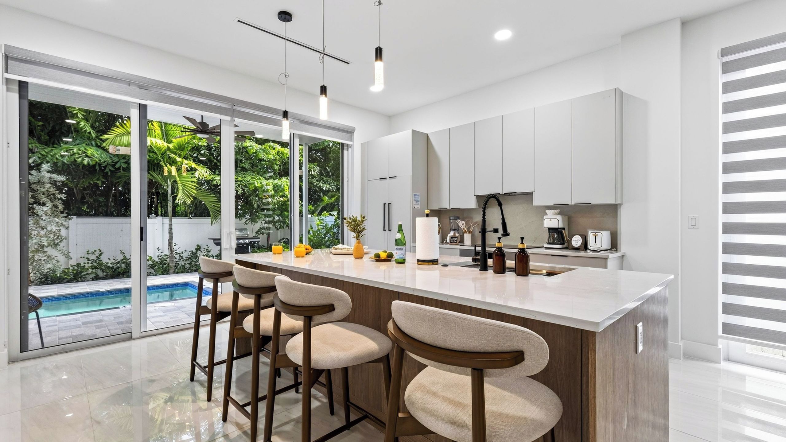 A modern kitchen with a large island, bar stools, and a view of a swimming pool.