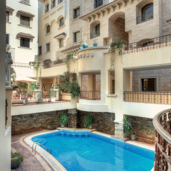 Un edificio de varios niveles con una piscina central rodeada de balcones con plantas y mobiliario exterior.