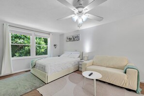 Ein Schlafzimmer mit Bett, Sofa, Nachttisch, Deckenventilator und einem Fenster mit Vorhängen.