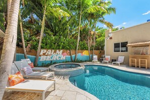 A pool area with lounge chairs and a hot tub, surrounded by palm trees and a mural reading "PALM BEACH". - Lux WPB Oasis with Heated Pool/Spa + GameRoom – Sleeps 12! (West Palm Beach)