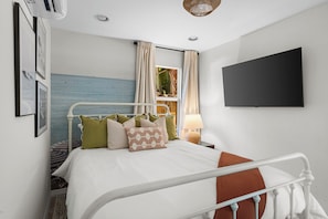 Ein modernes Schlafzimmer mit Bett, Fernseher und einem Fenster mit Vorhängen.
