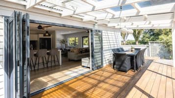 A modern house with a patio area featuring a dining table and chairs, a sliding glass door leading to an interior space with a kitchen and seating area.