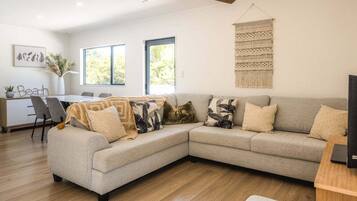 A modern living room with a sectional sofa, a dining area, and a large window providing natural light.