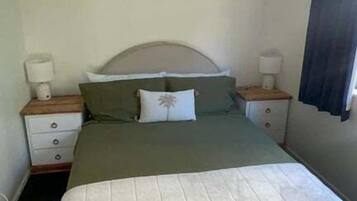 A single bed with a headboard, two bedside tables with lamps, a world map artwork on the wall, and a dark curtain on the window.
