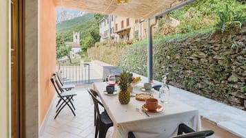 Zona pranzo all'aperto con tavolo imbandito per due, sedie e vista sul paesaggio circostante.