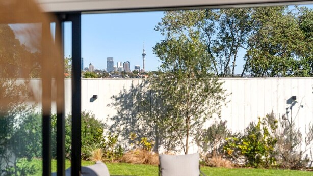 Blick aus einem Zimmer mit großem Fenster auf einen Garten und eine Stadtansicht.