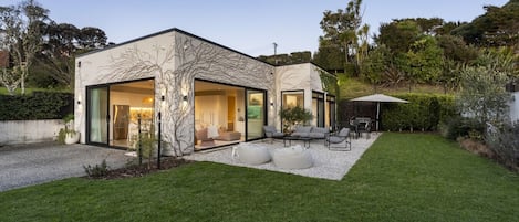 Une maison moderne avec une façade en verre, un patio doté de mobilier d’extérieur et une pelouse bien entretenue.