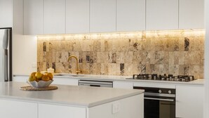 Eine moderne Küche mit weißen Schränken, einer Marmor-Spritzschutzwand, einem Gasherd und einer Obstschale auf der Arbeitsplatte.