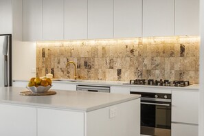 Eine moderne Küche mit weißen Schränken, einer Marmor-Spritzschutzwand, einem Gasherd und einer Obstschale auf der Arbeitsplatte.