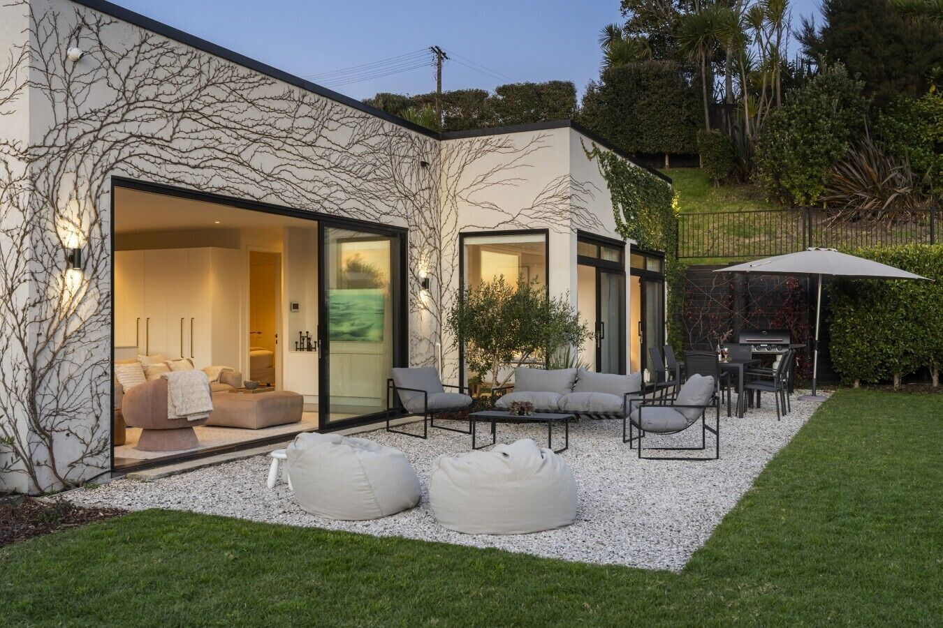 A modern house with a glass door leading to a living area, outdoor seating, and a barbecue setup.
