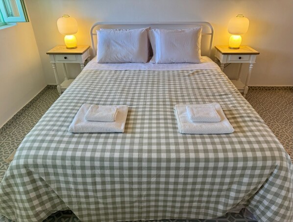 A neatly made bed with a checkered bedspread, two pillows, two bedside lamps, and two folded towels.