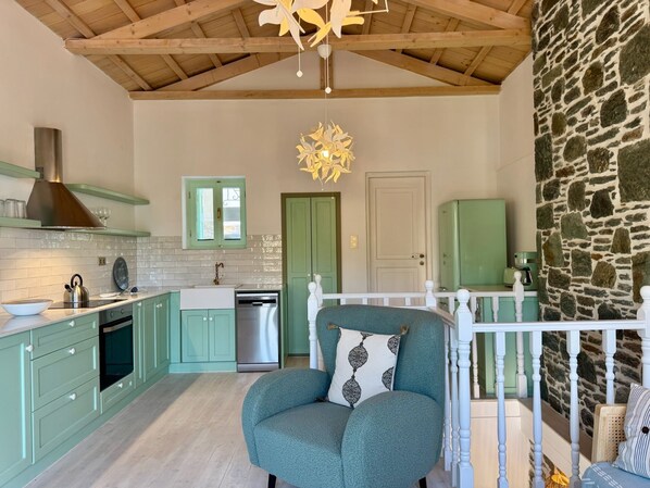 A spacious kitchen with a stone wall, a dining area with a white railing, and a cozy seating area with a teal armchair.