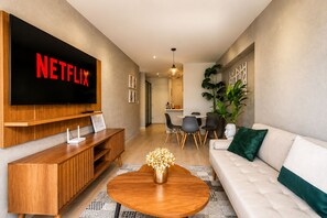 Una sala de estar moderna con televisor de pantalla plana, mueble de madera para entretenimiento, una mesa redonda para café y un sofá blanco.
