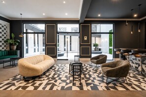 A modern lobby with a sofa, chairs, a bar area, and a patterned floor. - City Nest in Jesús María (Jesús María)
