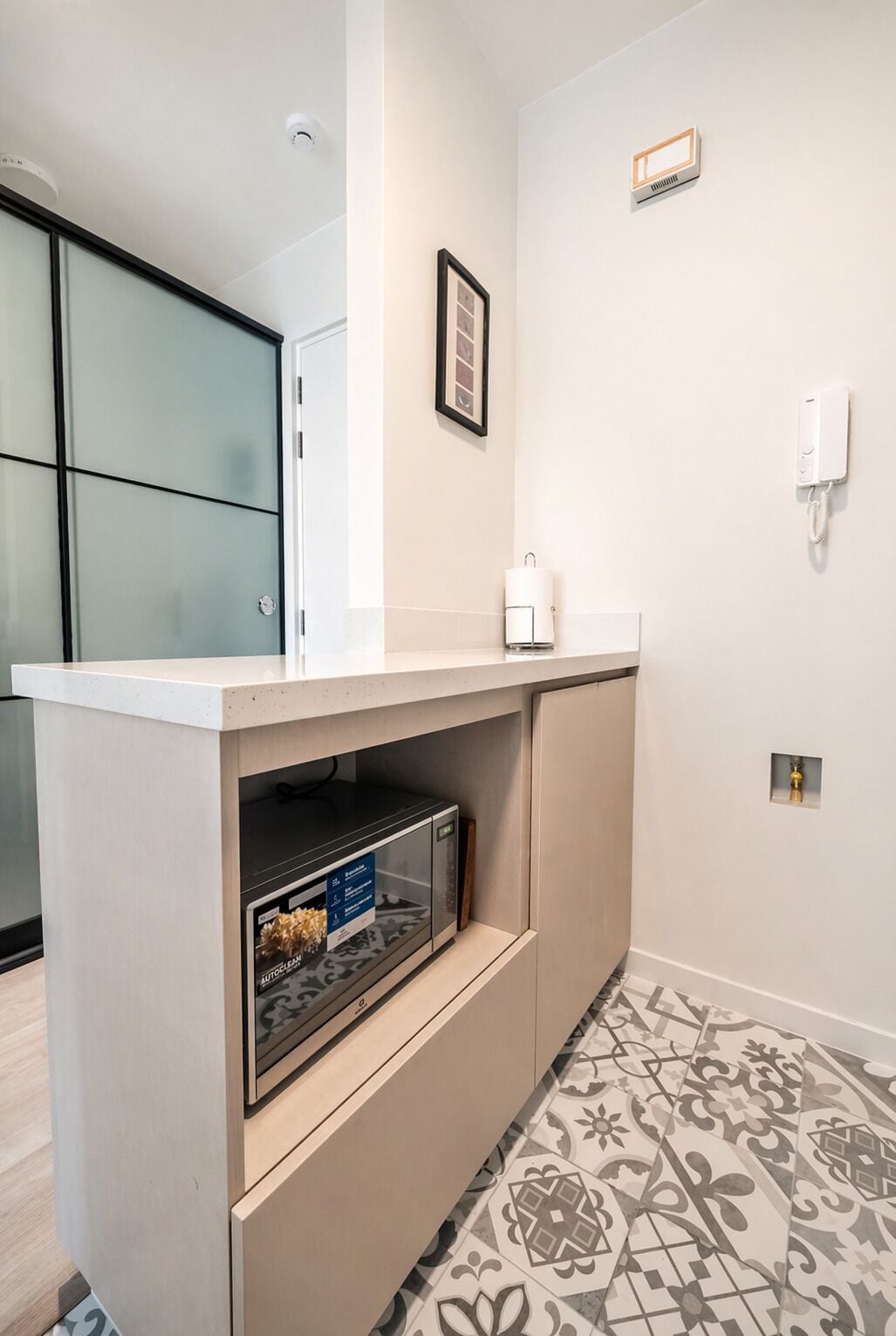 A kitchenette with a microwave, a small refrigerator, and a countertop. There is a framed picture on the wall and a wall-mounted phone.