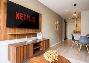 A modern living room with a large flat-screen TV mounted on the wall, a wooden entertainment unit below, a round coffee table with a decorative bowl, and a dining area with chairs and a table in the background. - City Nest in Jesús María (Jesús María)