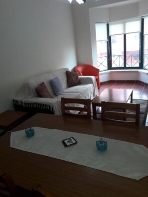 Una habitación con sofá, una silla roja, una mesa de madera y ventana con vistas.