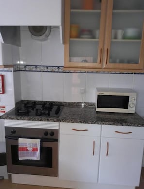 Una cocina con estufa, horno, microondas y armarios blancos con tiradores de madera.