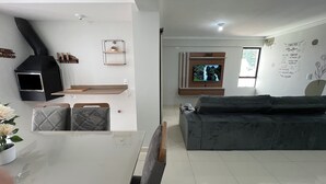 A modern living room with a sofa, a dining table with chairs, a kitchen area with a stove, and a television mounted on the wall. - Family apartment with great comfort and a great location in Toledo, Paraná. (Toledo)