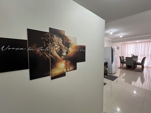 A dining area with a table and chairs, a refrigerator, and a wall with three framed artworks.