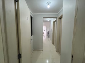 A hallway with a tiled floor leading to a room with a bed and a window.