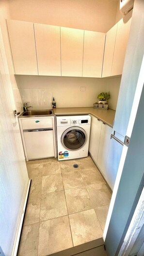 A compact laundry room with a washing machine, a sink, and cabinets. - ObanLee Country Retreat a Luxurious Country Getaway to Relax, Reconnect & Unwind (Tallegalla)