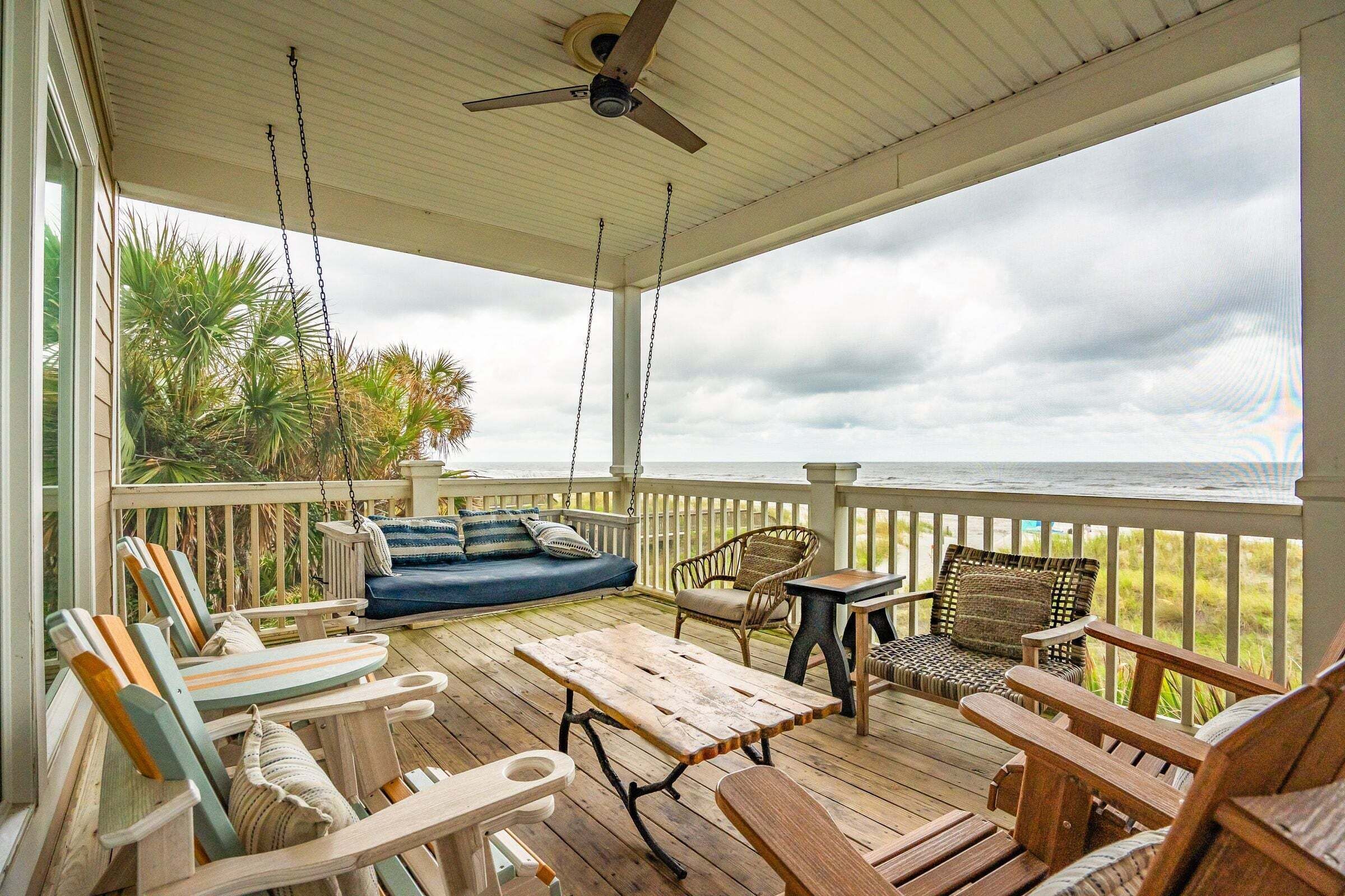A covered outdoor deck with seating, a table, and a view of the ocean.