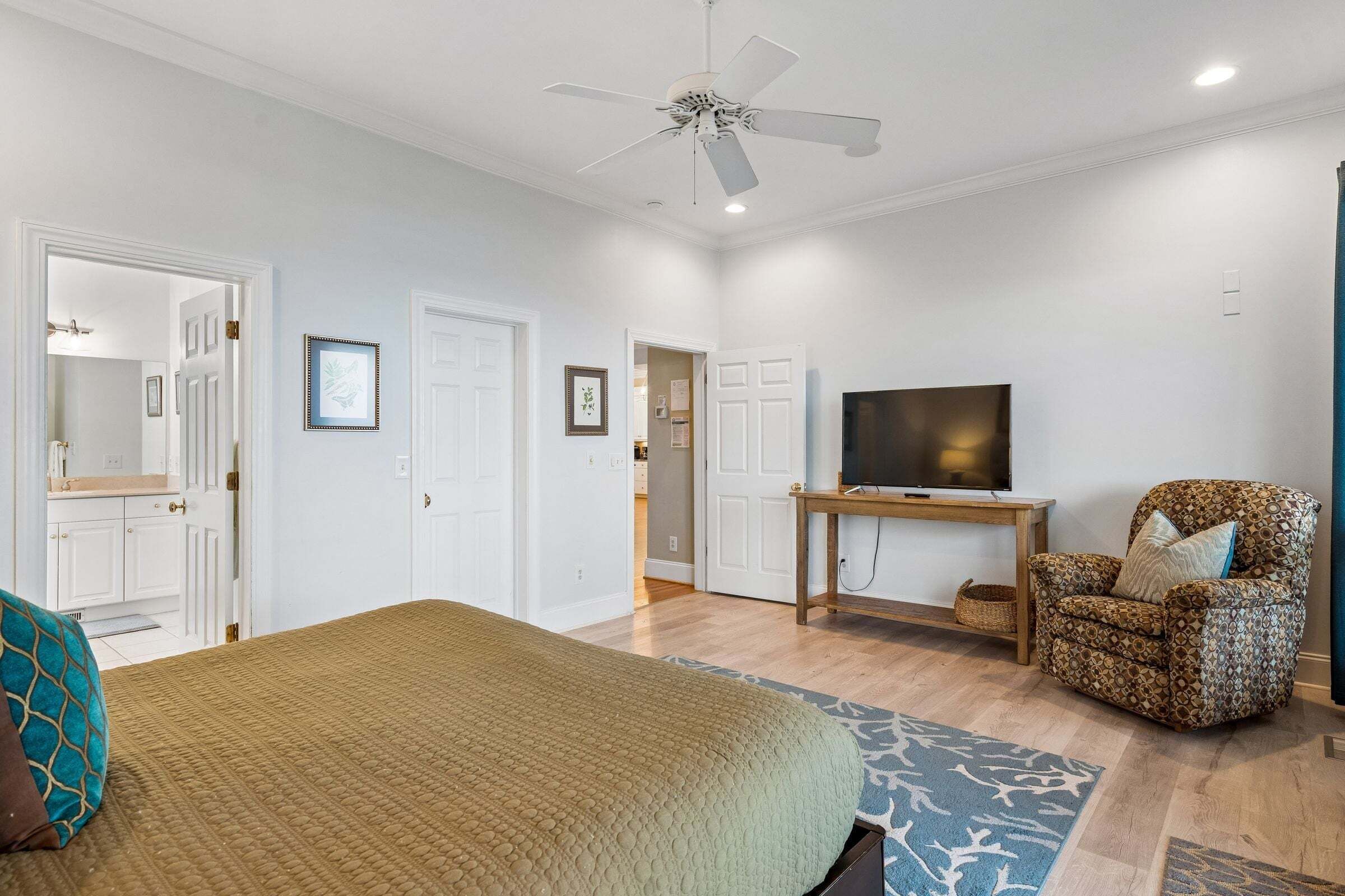 Un dormitorio con una cama, televisión, silla y ventilador de techo.