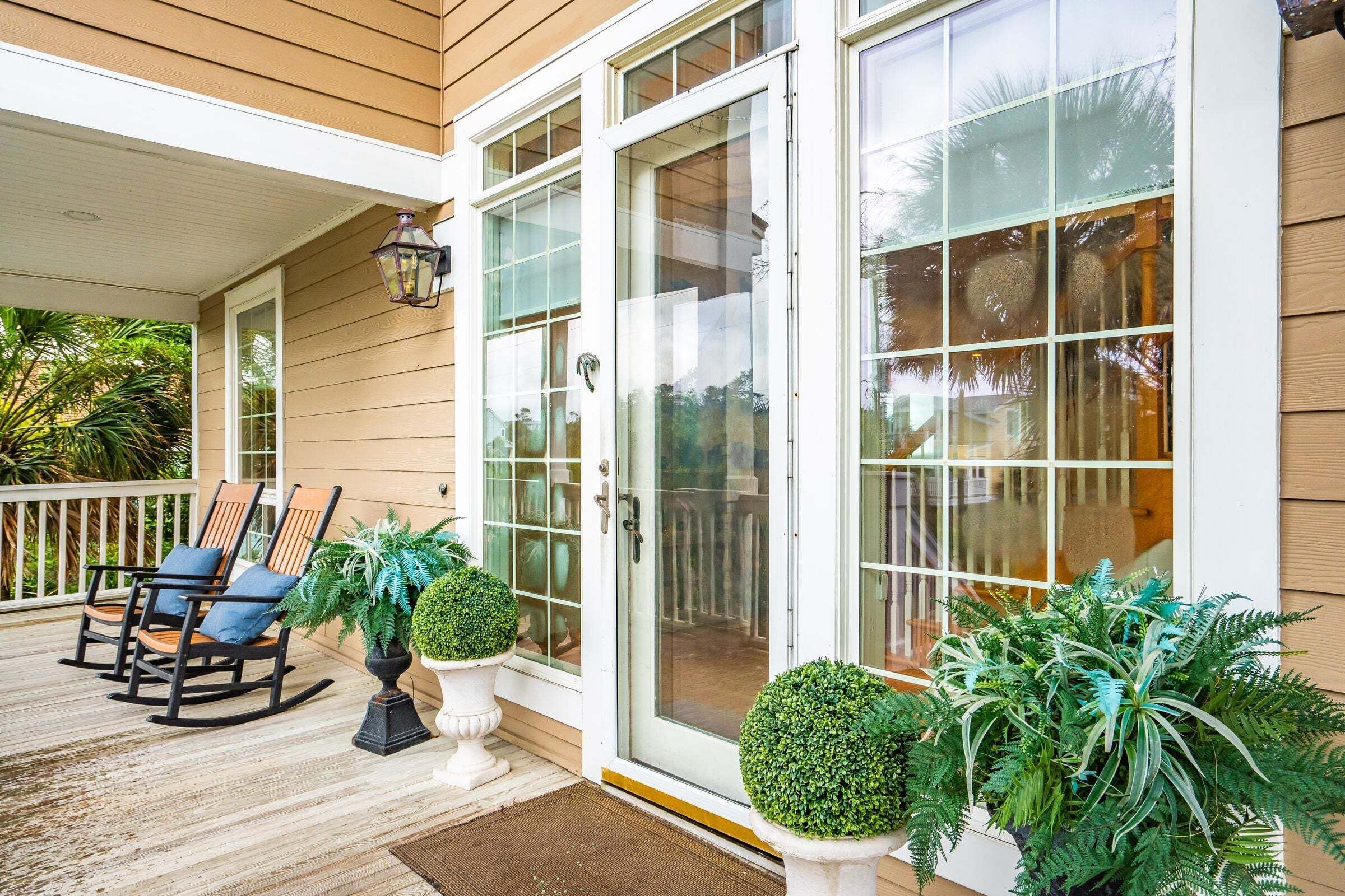 A covered porch with rocking chairs and potted plants, a glass door entrance, and a wooden exterior.