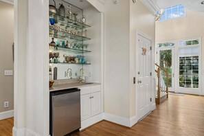 A kitchen with a built-in dishwasher, a glass-fronted display shelf with various glassware, and a door with a 'Do Not Enter' sign. - Gypsy Tide! Luxury 5 BR, 5.5 BA Oceanfront Home-Folly Beach! (Folly Beach)