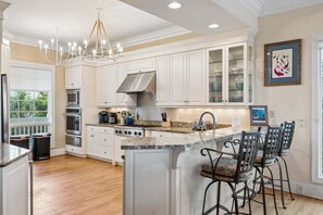 A spacious kitchen with white cabinetry, a central island with bar stools, stainless steel appliances, and a chandelier. - Gypsy Tide! Luxury 5 BR, 5.5 BA Oceanfront Home-Folly Beach! (Folly Beach)