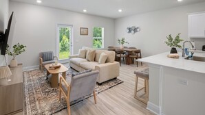A modern living room with a sofa, a dining table, and a kitchen area with a sink and countertop.