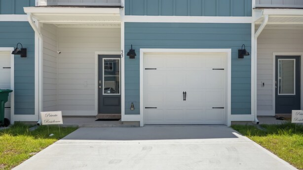 A two-story residential building with a central garage door, a small porch with a door, and a clear sky above.