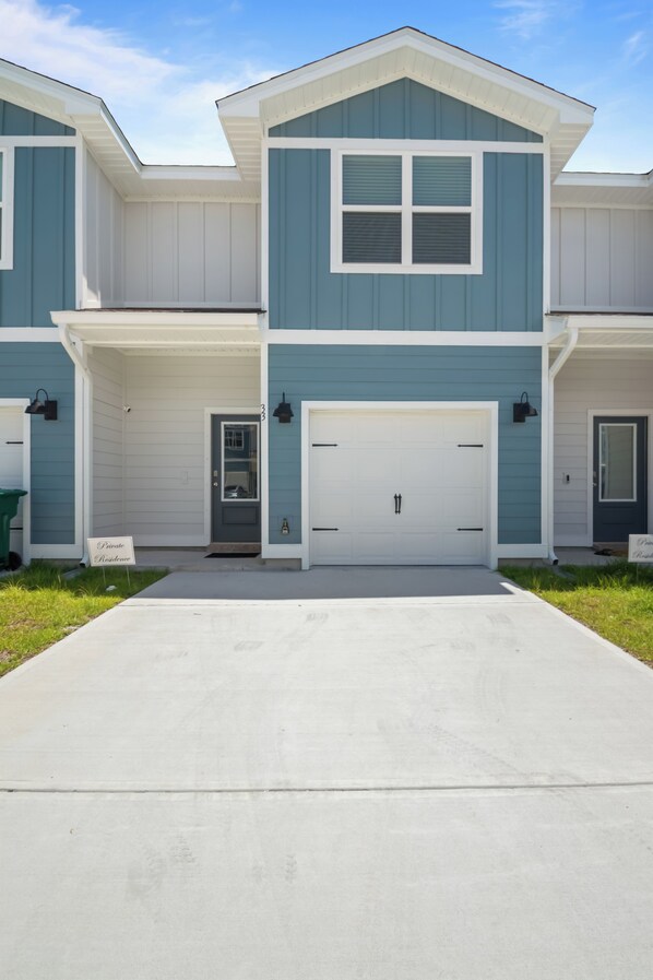 A two-story residential building with a central garage door, a small porch with a door, and a clear sky above.