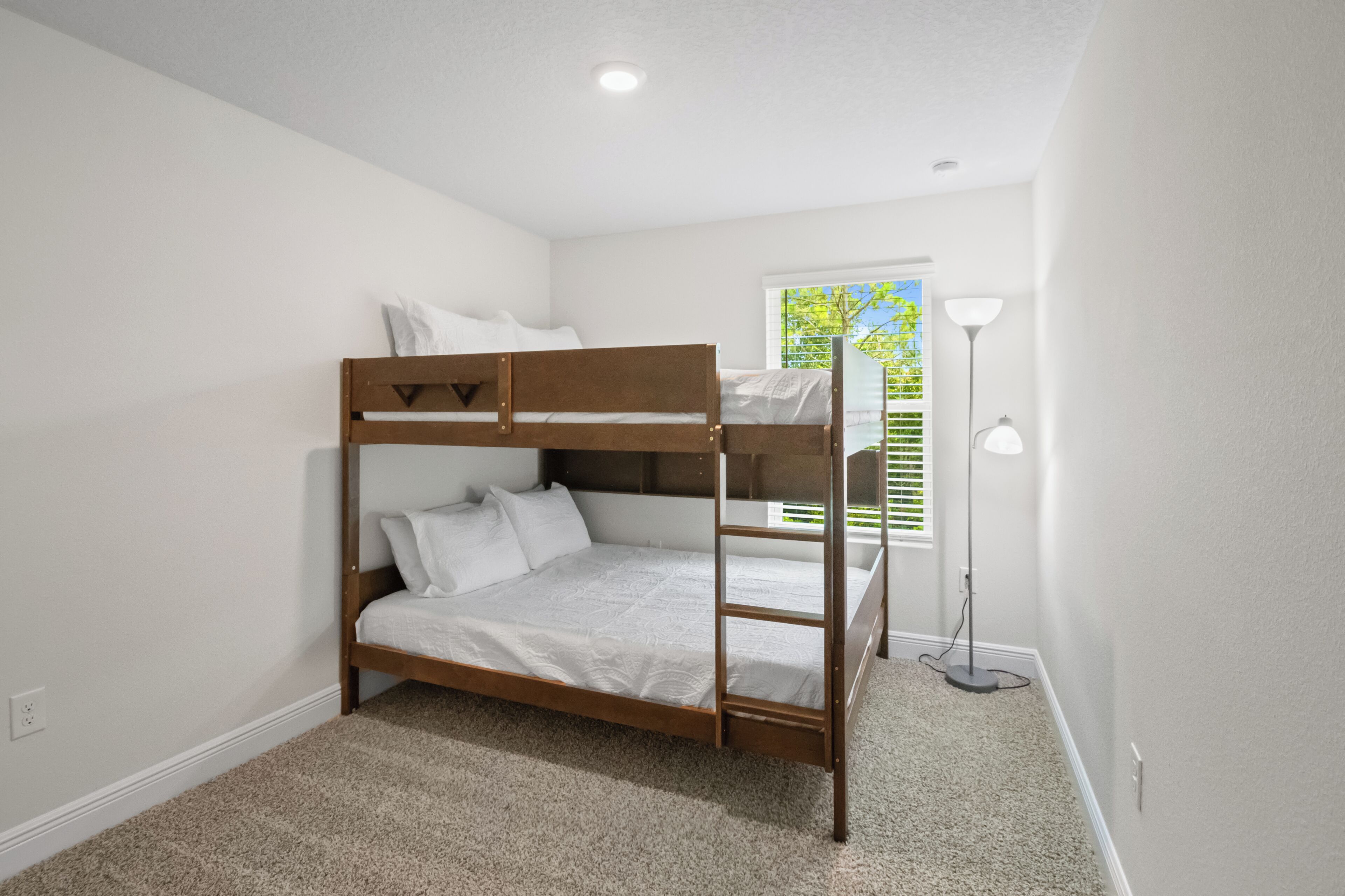 A bunk bed in a room with white walls, a carpeted floor, and a window with blinds.