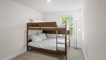 A bunk bed in a room with white walls, a carpeted floor, and a window with blinds.