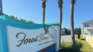 A sign for Forest Shores Villas with a clear view of the surrounding area including a road and a building.