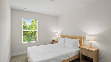 Un dormitorio con una cama, dos mesitas de noche con lámparas, una ventana con persianas y suelo alfombrado.