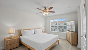 A bedroom with a bed, nightstands, a ceiling fan, a window with blinds, and a door.