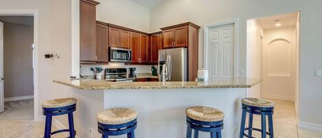 A kitchen with a central island, wooden cabinets, stainless steel appliances, and blue stools.