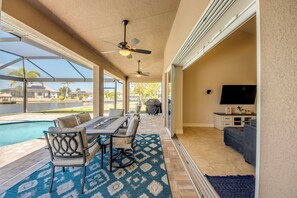 An outdoor patio with a pool, a covered dining area, and a TV on the right. - Fantastic 4-bedroom house with Heated Saltwater Pool & Spa (Cape Coral)