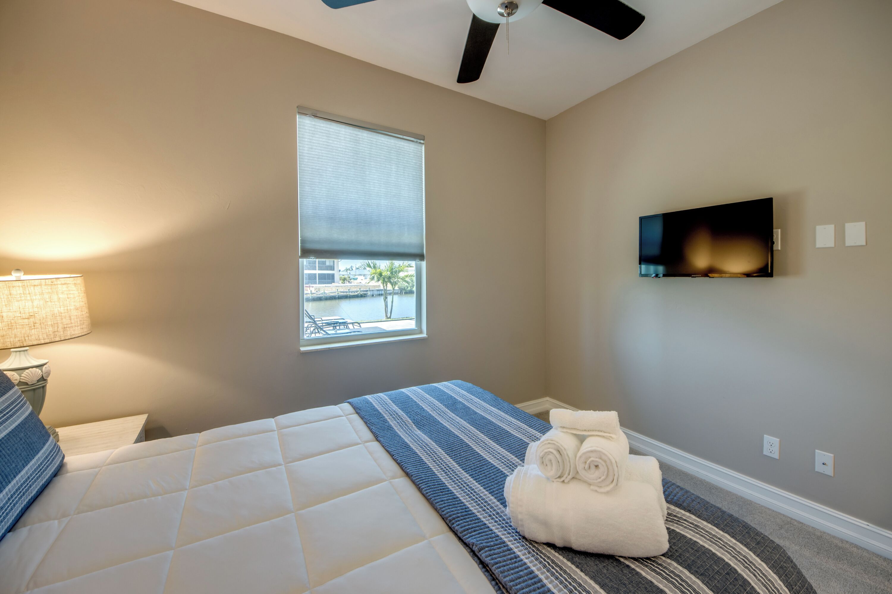 Habitación de hotel con cama, ventilador de techo, ventana, televisor de pantalla plana y vista al exterior.