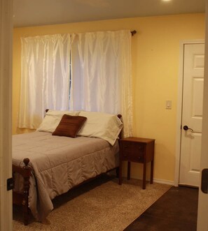 Une chambre à coucher avec un lit, une table de chevet, une porte et une fenêtre avec des rideaux.
