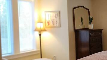 Een slaapkamer met een bed, nachtkastje, lamp, kaptafel en raam.