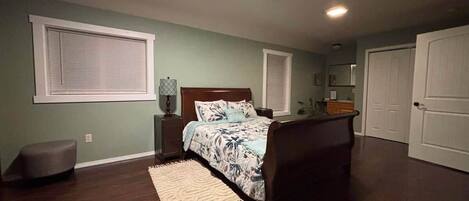 Un dormitorio con cama, mesitas de noche, alfombra, banco y una puerta.