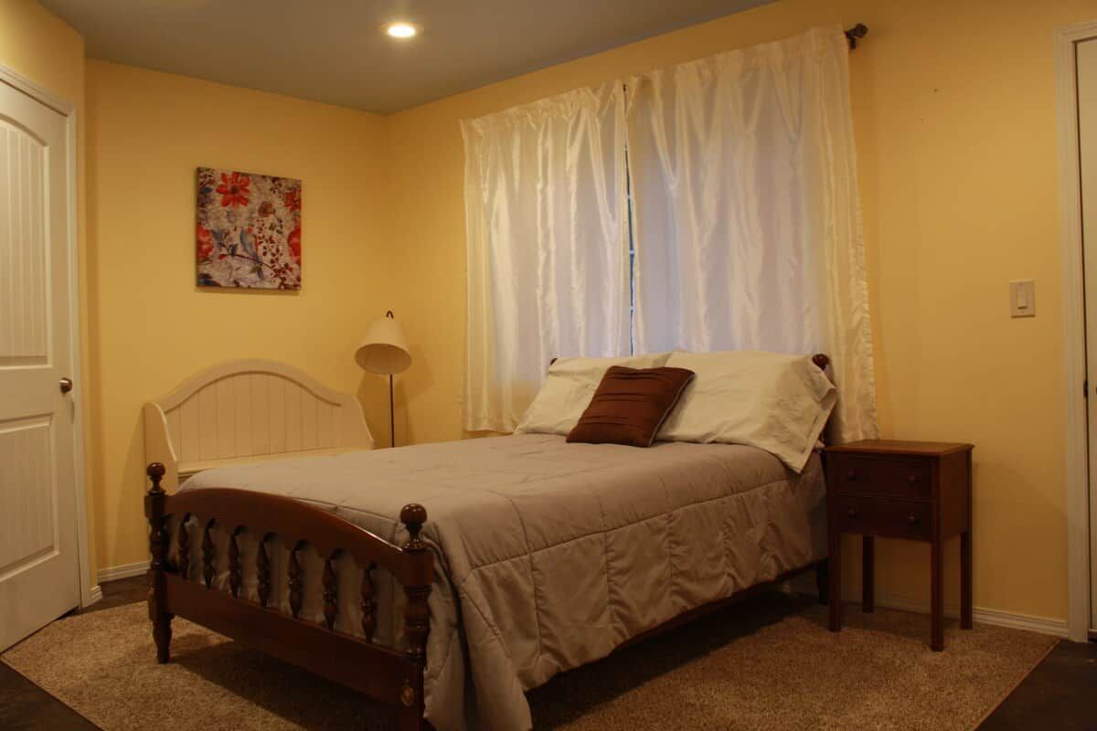 A bedroom with a bed, a bedside table, a lamp, a door, and a wall with a painting.