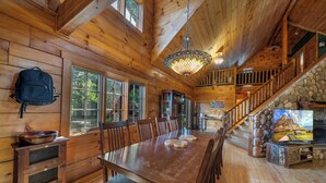L’intérieur d’un chalet en bois comprend une table à manger, des chaises, un escalier et un lustre.