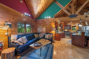 L’intérieur chaleureux d’un chalet, avec un revêtement en bois, un canapé bleu, un coin cuisine et une vue par les fenêtres.