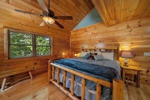 Ein Schlafzimmer einer Holzhütte mit einem Bett, einem Deckenventilator, einem Fenster und einem Nachttisch mit einer Lampe.