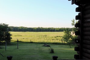 A view of a grassy field with a fence, trees, and a building in the background. - Log Cabin with Twin Ponds Near Letchworth State Park (Nunda)